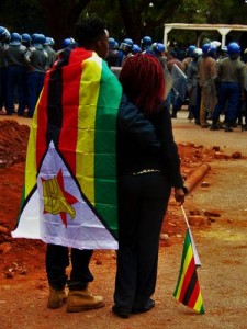 A young couple with flags watches warily as riot police assemble outside the Magistrates’ Court